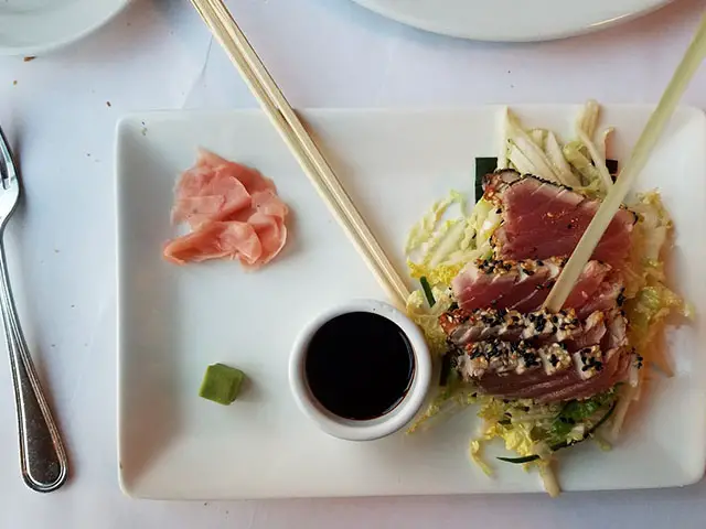 raw fish served with salad and sauce on a white plate